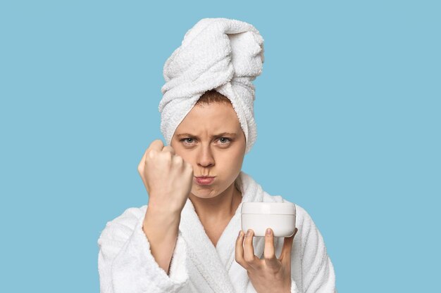 Photo young caucasian redhead presenting cream showing fist to camera aggressive facial expression