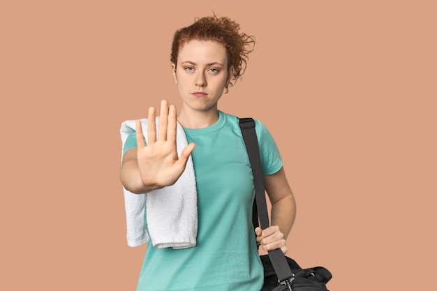 Young Caucasian redhead with gym gear standing with outstretched hand