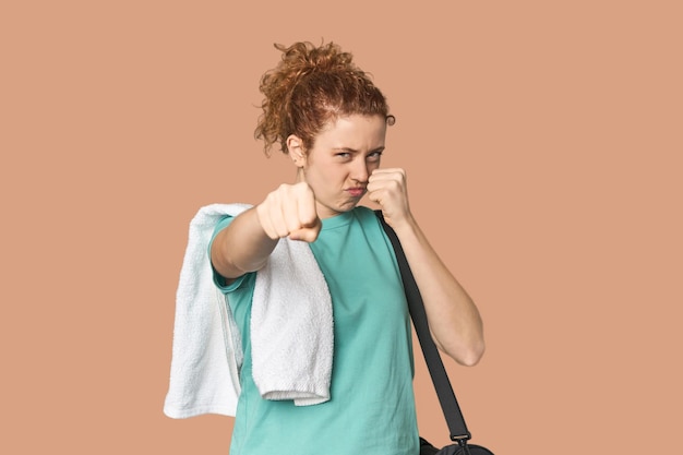 Young Caucasian redhead with gym gear throwing a punch anger fighting due to an argument boxing