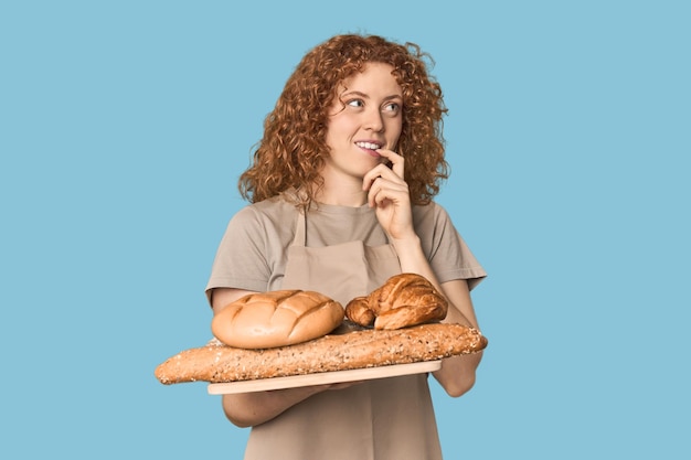 Photo young caucasian redhead woman holding bread tray relaxed thinking about somethin