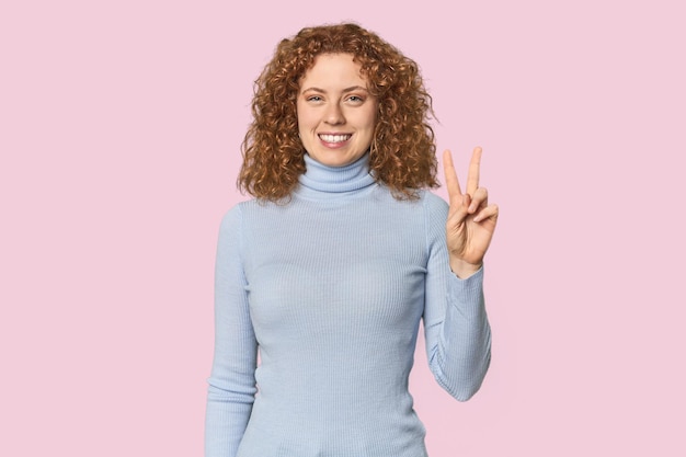 Young Caucasian redhead woman showing victory sign and smiling broadly