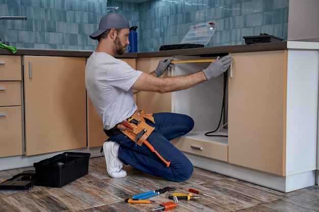 Young caucasian repairman measuring size of kitchen drawer