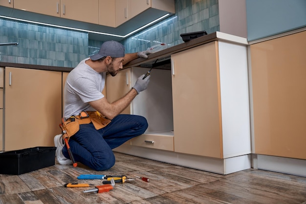 Young caucasian repairman screwing new kitchen furniture