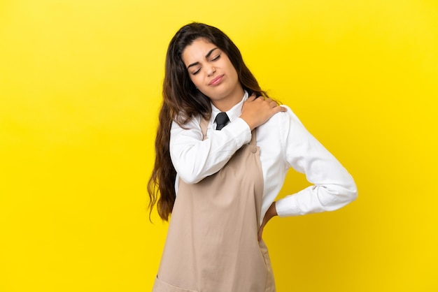 Young caucasian restaurant waiter isolated on yellow background suffering from pain in shoulder for having made an effort