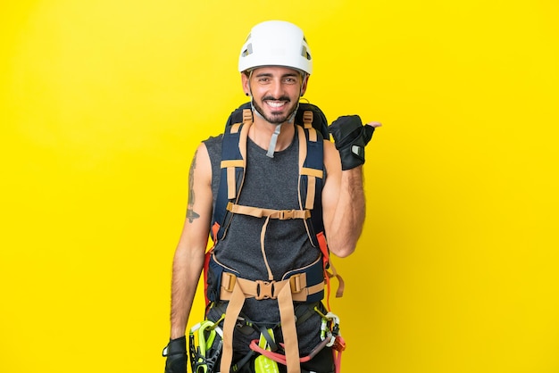 Young caucasian rock climber man isolated on yellow background pointing to the side to present a product