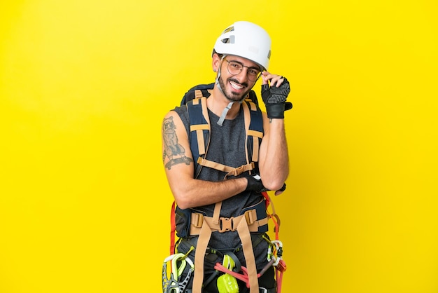 Young caucasian rock climber man isolated on yellow background\
with glasses and happy