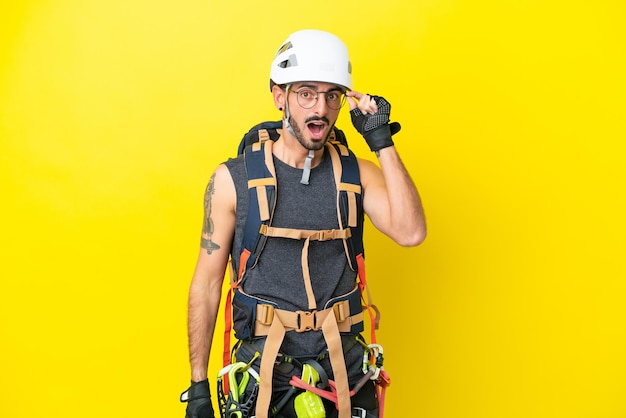 Young caucasian rock climber man isolated on yellow background with glasses and surprised