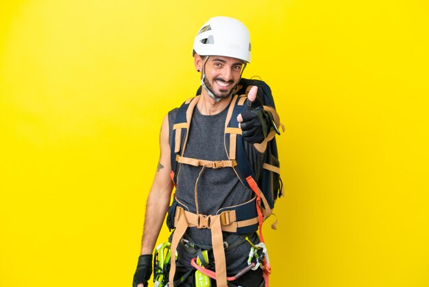 Young caucasian rock climber man isolated on yellow background with thumbs up because something good has happened