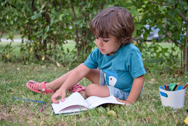 Young caucasian school boy sitting in park outdoor doing school
homework child kid writing in notebook with pencil outside self
education learning studying early development for children