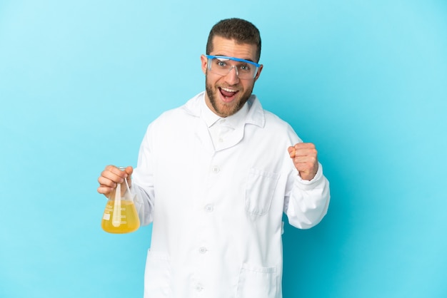 Young caucasian scientific man isolated on blue wall celebrating a victory in winner position