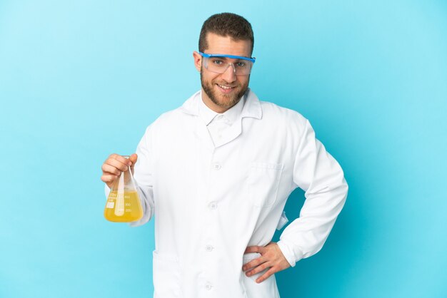 Young caucasian scientific man isolated on blue wall posing with arms at hip and smiling