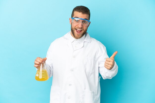 Young caucasian scientific man isolated on blue wall with thumbs up because something good has happened