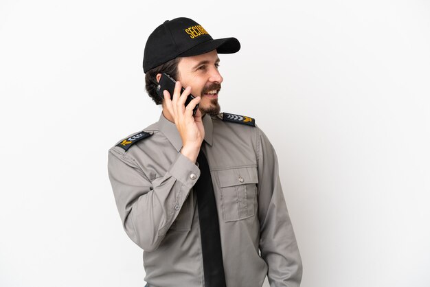 Young caucasian security man isolated on white background keeping a conversation with the mobile phone with someone