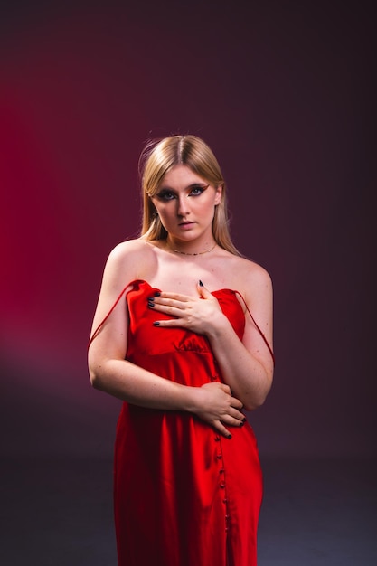 Young caucasian sexy woman with a red dress on a photography studio with a black background with a red light.