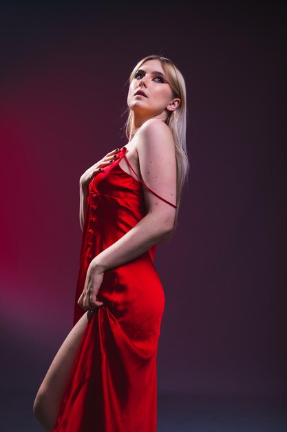 Young caucasian sexy woman with a red dress on a photography studio with a black background with a red light.