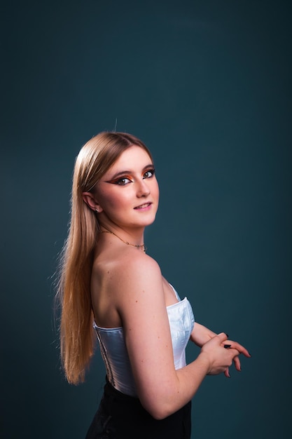 Young caucasian sexy woman with a white corset and black trousers in a photography studio with a blue dark background.