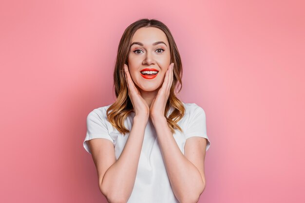 Young caucasian shocked woman in a white t-shirt smiling looking directly isolated on pink background