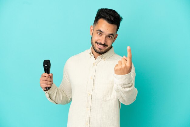 Молодой кавказский певец мужчина изолирован на синем фоне, делая приближающийся жест