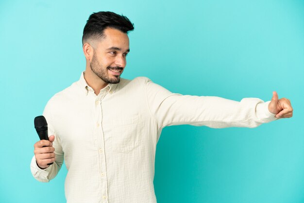 Young caucasian singer man isolated on blue background giving a thumbs up gesture