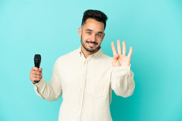 Young caucasian singer man isolated on blue background happy and counting four with fingers