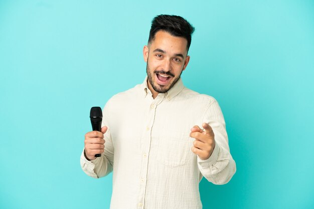 Young caucasian singer man isolated on blue background surprised and pointing front