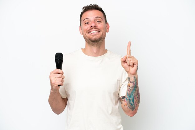 Young caucasian singer man picking up a microphone isolated on white background pointing up a great idea