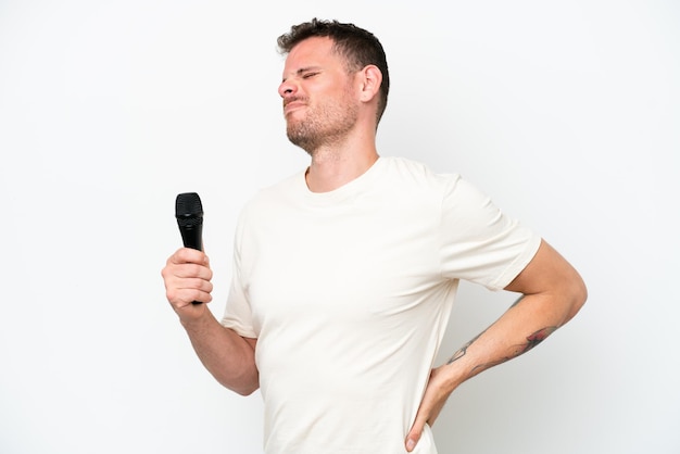 Young caucasian singer man picking up a microphone isolated on white background suffering from backache for having made an effort