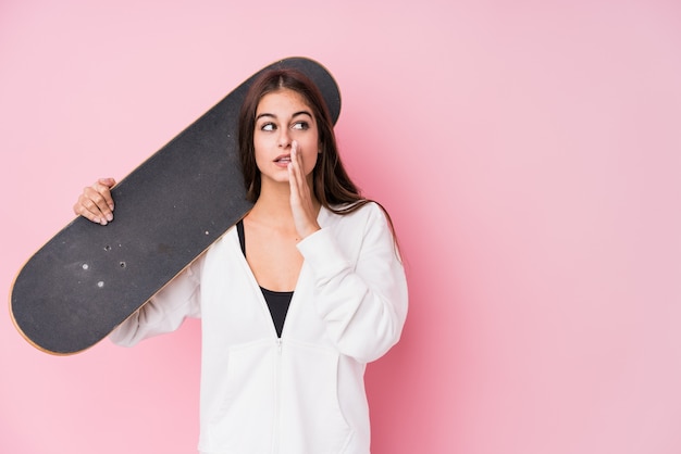 Young caucasian skater woman holding skate is saying a secret hot braking news and looking aside