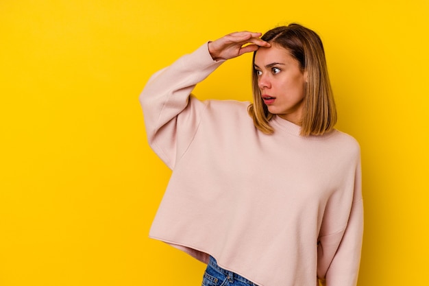 Young caucasian skinny woman isolated on yellow looking far away keeping hand on forehead.