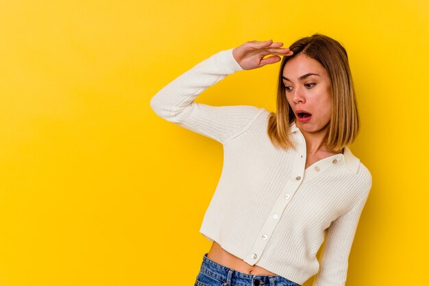 Young caucasian skinny woman isolated on yellow looking far away keeping hand on forehead.