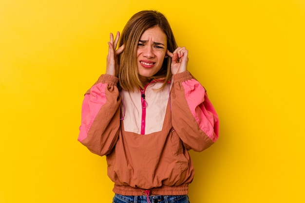 指で耳を覆う黄色の壁に隔離された若い白人の細い女性は、大声で周囲の環境によってストレスと絶望的