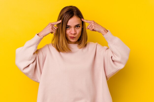 Young caucasian skinny woman isolated on yellow wall focused on a task, keeping forefingers pointing head.