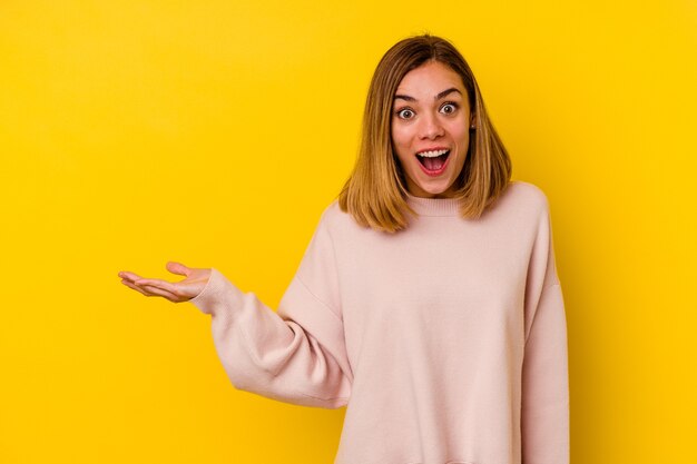 Young caucasian skinny woman isolated on yellow wall impressed holding copy space on palm