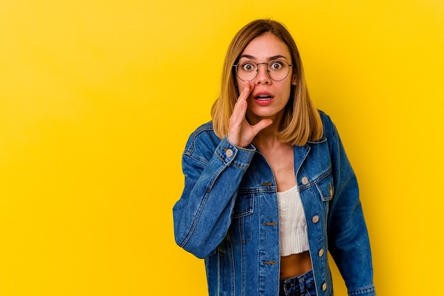 Young caucasian skinny woman isolated on yellow wall is saying a secret hot braking news and looking aside