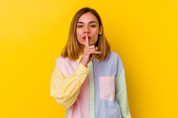 Young caucasian skinny woman isolated on yellow wall keeping a secret or asking for silence.