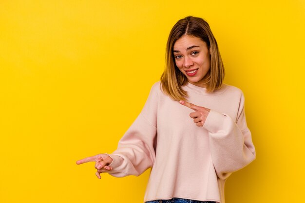 Giovane donna magra caucasica isolata sulla parete gialla scioccata che punta con il dito indice a uno spazio di copia