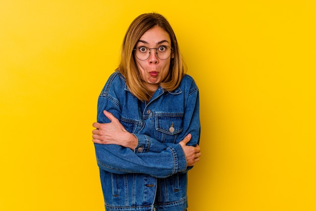 Young caucasian skinny woman isolated on yellow wall shrugs shoulders and open eyes confused.