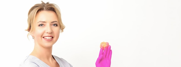 Young caucasian smiling female beautician holding wax for depilation over white background yellow sugar paste in hands master of depilation epilation concept