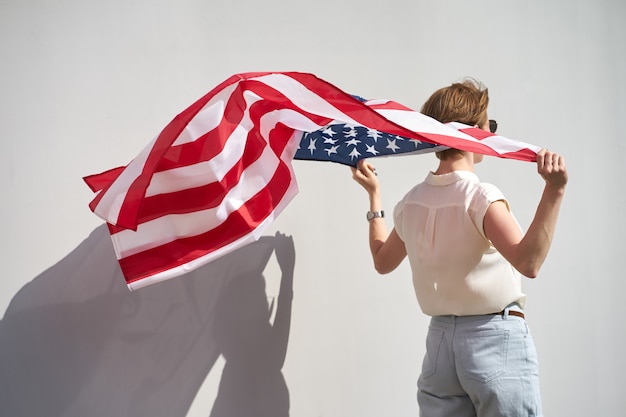 写真 風になびくマントのようなアメリカ国旗の後ろに保持しているサングラスの若い白人笑顔の女の子