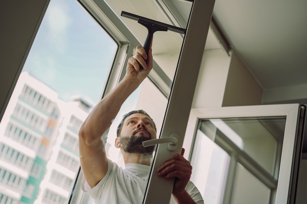 young caucasian smiling man washing the window with a squeegeeCleaning concept