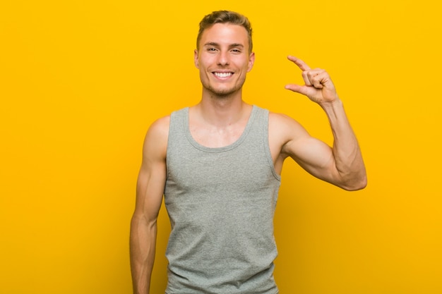 Young caucasian sport man holding something little with forefingers, smiling and confident.