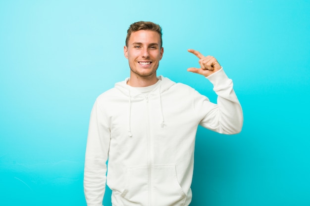 Young caucasian sport man holding something little with forefingers, smiling and confident.