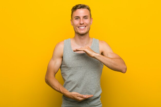 Uomo caucasico giovane di sport che tiene qualcosa con entrambe le mani, presentazione del prodotto.