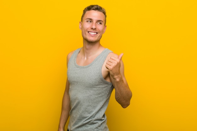 Young caucasian sport man points with thumb finger away, laughing and carefree.