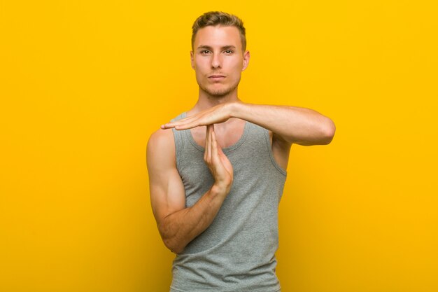 Young caucasian sport man showing a timeout gesture.