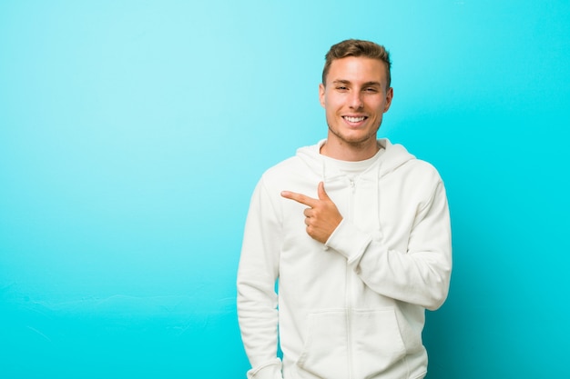 Young caucasian sport man smiling and pointing aside, showing something at blank space.