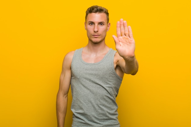 Young caucasian sport man standing with outstretched hand showing stop sign, preventing you.