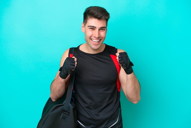 Young caucasian sport man with sport bag isolated on blue background celebrating a victory in winner position