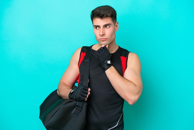 Young caucasian sport man with sport bag isolated on blue background having doubts and thinking