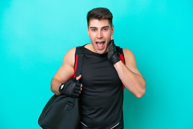 Young caucasian sport man with sport bag isolated on blue background with surprise and shocked facial expression